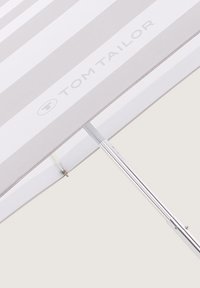 Parasol rayé en tissu gris clair et blanc, avec un cadre en métal argenté, un mât télescopique et un détail de logo.