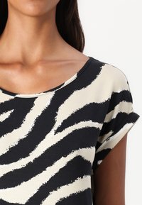Camiseta de manga corta en negro y crema con un patrón de rayas de cebra; tejido suave, ajuste relajado, escote más amplio, mangas enrolladas.