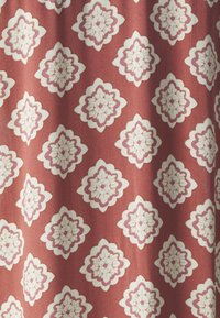 Textil függöny vörös háttérrel, amelyen krémszínű és világoslila virágminták ismétlődnek, texturált megjelenéssel.