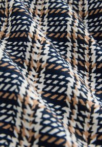 Tissu tissé présentant un motif géométrique en bleu marine, blanc et beige, avec une surface texturée offrant une qualité tactile.