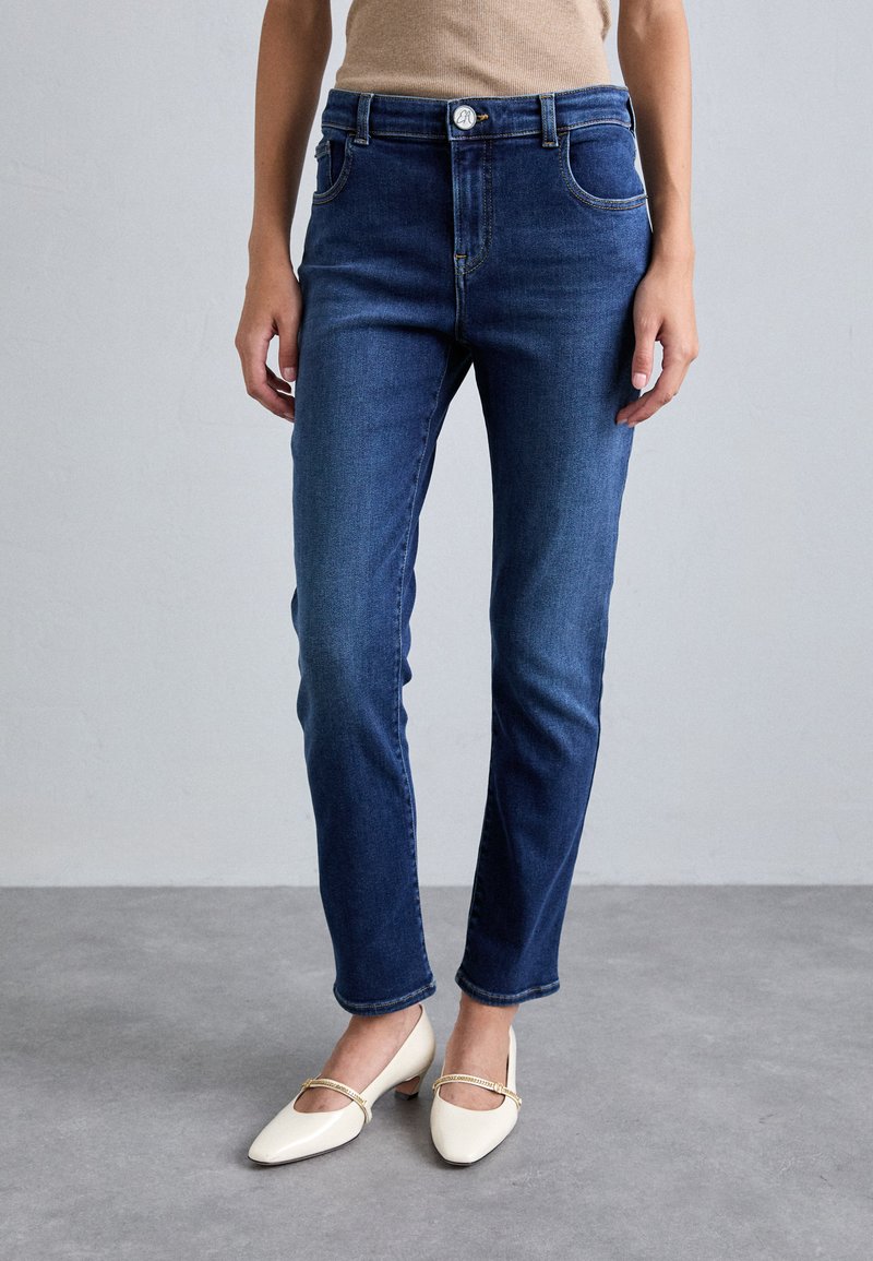 Μπλε τζιν παντελόνι με σλιμ εφαρμογή, πέντε τσέπες και διακριτές λεπτομέρειες ραφής. Το ύφασμα έχει λεία υφή και ελαφριά ελαστικότητα.