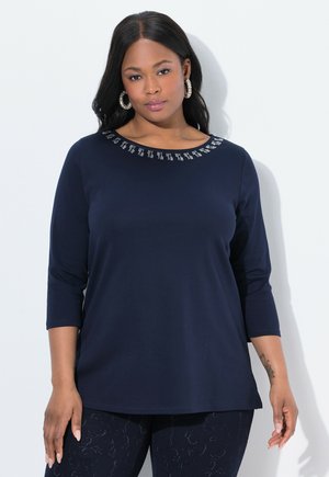 Marineblaues Langarmshirt mit rundem Ausschnitt, verziert mit kleinen silbernen Details entlang des Kragens. Weicher, dehnbarer Stoff. Lässige Passform.