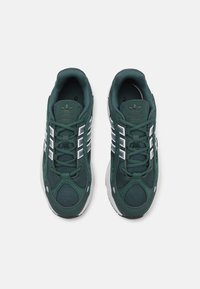 Green mesh sneakers featuring three white stripes, padded lace area, reinforced toe, and a textured sole. Branding on the tongue.