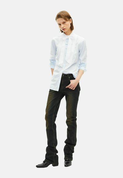 Light blue striped shirt with bow tie detail, paired with dark jeans and black boots. The fabric appears smooth; the fit is tailored.