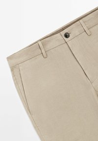 Beige Leinenhosen mit flacher Vorderseite, Gürtelschlaufen und einem einzelnen Knopfverschluss. Sie verfügen über eine dezente Textur und klare, maßgeschneiderte Linien.