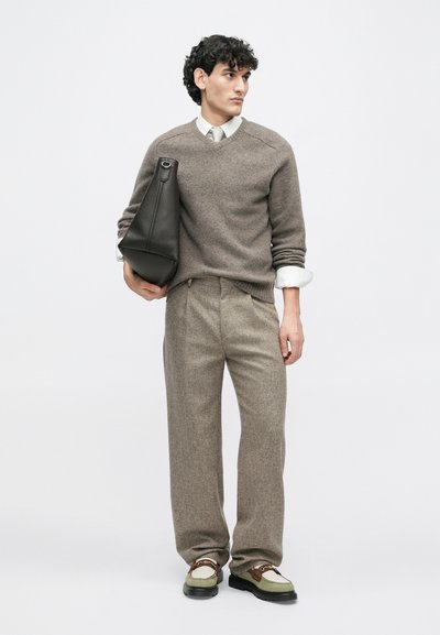 Maglione marrone a maglia, camicia chiara, pantaloni a scacchi marroni e borsa in pelle nera. Scarpe con accenti verdi e marroni e suola spessa.