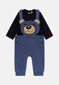 Marineblaue Langarmshirt, kombiniert mit blauen Latzhosen mit einem Bärenkopf-Design. Die Latzhosen haben Schulterträger und Druckknopfverschlüsse.