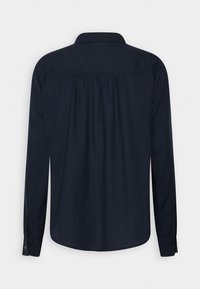 Chemise bleu marine à manches longues avec un col et des plis froncés sur le haut du dos, vue de dos sur un fond uni.