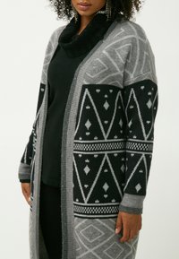 Larga chaqueta de punto con un patrón geométrico en negro y gris, con una textura suave de mezcla de lana y un cuello tipo cowl.