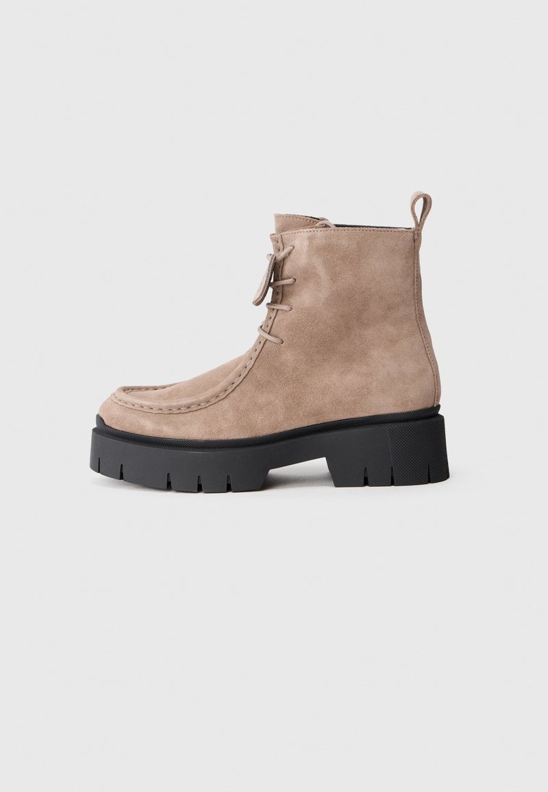 Bottine en daim marron clair avec lacets à l'avant, languette arrière et semelle noire épaisse et robuste avec des crampons profonds.