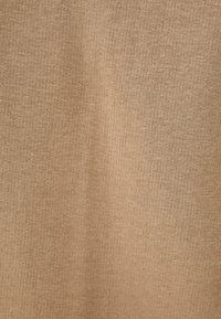 Beżowa dzianina o gładkiej teksturze i drobnym splocie, z subtelnymi odcieniami koloru i jednolitym wzorem na całej powierzchni.