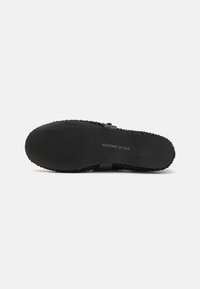 Black slide sandal with textured surface and a smooth, flat sole. Features a wide strap for support and a simple design.