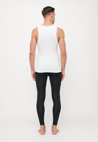 Hvid tanktop og sorte leggings båret af en mandlig model, der fremviser et tætsiddende design og glat stoftekstur, uden synlige mønstre.
