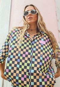 Chemise à manches courtes avec un motif à carreaux multicolores en noir, rose, bleu, vert et orange. Comprend un petit écusson logo et des boutons.
