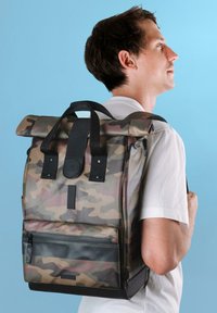 Zaino roll-top con motivo camouflage in toni terrosi smorzati, dotato di spallacci neri, una tasca frontale con zip e una base rinforzata per una maggiore durata.
