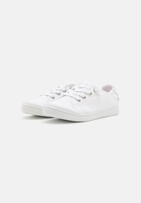 Un paio di sneakers casual bianche con tessuto testurizzato, lacci bianchi e suole in gomma bianche su uno sfondo chiaro e semplice.