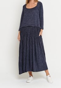 Marinblå stickad topp med en vid rundad halsringning, kombinerad med en plisserad långkjol i matchande tyg. Bärs med vita sneakers.