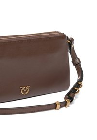 Smeđa kožna torba preko tijela s zlatnim detaljima, zatvaranjem na zašitak i dekorativnim logotipom. Ima teksturiranu naramenicu i glatku površinu.