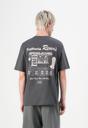 Person with short blond hair wearing a dark gray T-shirt featuring an illustrated trattoria storefront and text on the back.