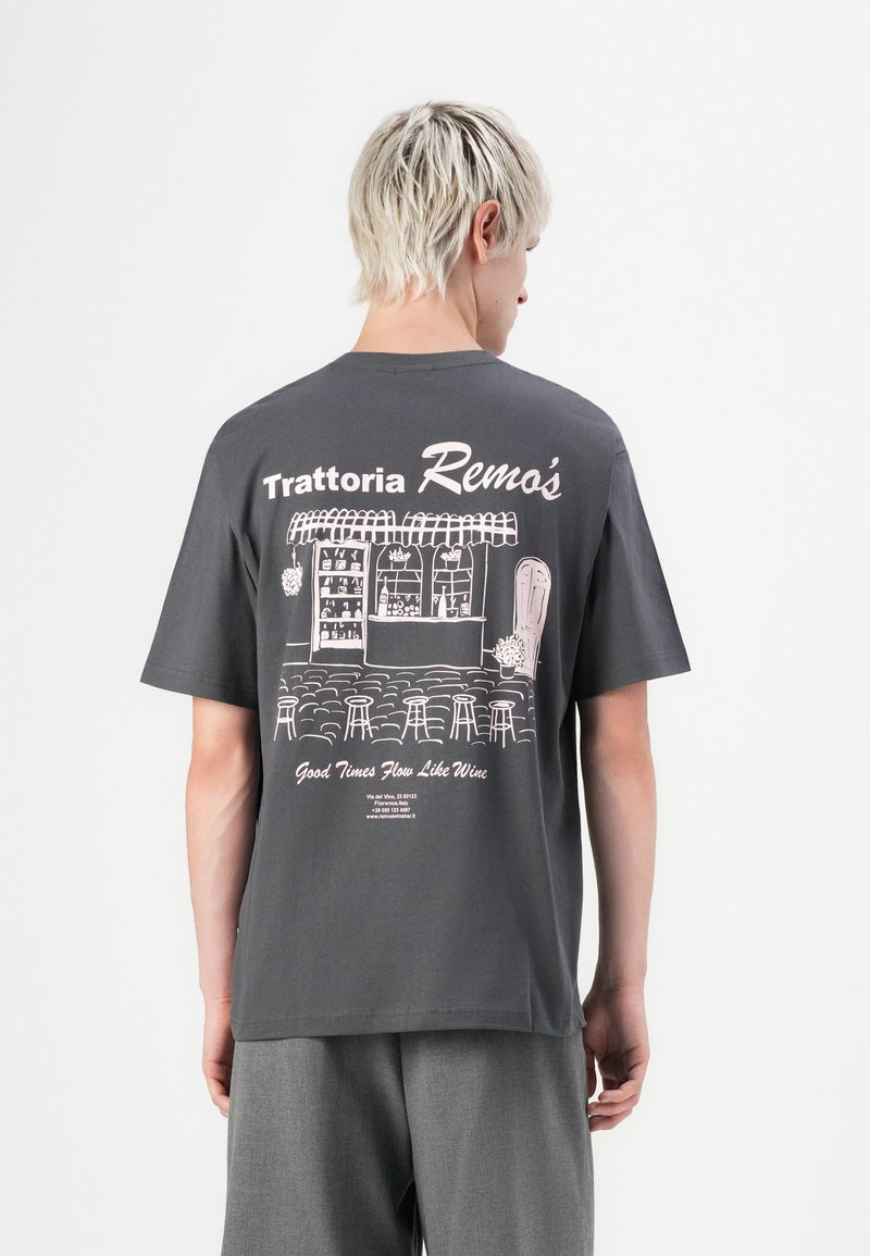 Person with short blond hair wearing a dark gray T-shirt featuring an illustrated trattoria storefront and text on the back.