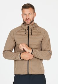 Giacca leggera, di colore beige, imbottita, con chiusura lampo, cappuccio con coulisse, dettagli neri e polsini elastici. Presenta dettagli riflettenti sulle maniche.