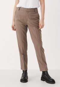 Bruna skräddarsydda byxor med rak benstil, med framveck och sidofickor, i kombination med svarta ankelstövlar.