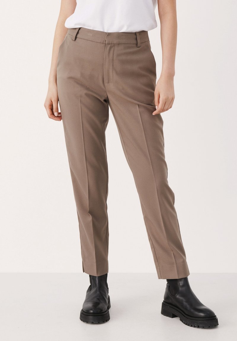 Bruna skräddarsydda byxor med rak benstil, med framveck och sidofickor, i kombination med svarta ankelstövlar.