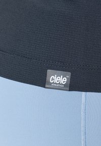 Athletiske shortser i lyseblått stoff med en teksturert mørkeblå linning som har en fremtredende "ciele ATHLETICS" etikett.