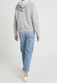 Jasnoszara bluza z kapturem z białym wnętrzem i regulowanym sznurkiem, zestawiona z jasnoniebieskimi dżinsami z poszarpanymi końcami. Białe trampki.