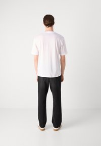 Camiseta blanca de manga corta, fabricada en algodón, de corte recto, combinada con pantalones de pierna ancha negros y zapatillas blancas con suela marrón claro.