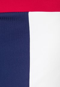 Tejido en bloque de colores que presenta rojo en la parte superior, seguido de azul marino con textura acanalada, y una sección blanca lisa.