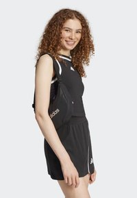 Débardeur de sport noir avec des accents blancs, shorts noirs et un petit sac bandoulière noir arborant le logo Adidas en blanc.