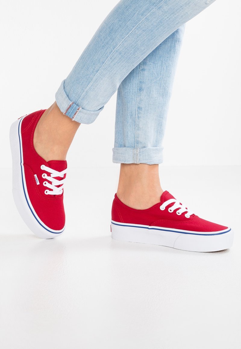 Jambes en jean bleu clair retroussées portant des baskets plateformes rouges en toile avec des lacets blancs et des semelles blanches épaisses.