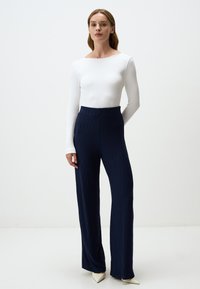 Top bianco a maniche lunghe con costine abbinato a pantaloni a vita alta blu navy a gamba larga con texture a costine verticali. Classiche décolleté bianche a punta.