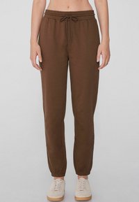 Braune Sweatpants mit elastischem Bund und Kordelzug, mit Bündchen an den Knöcheln und Seitentaschen, kombiniert mit hellen Sneakers.