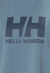 Camiseta de color azul claro con una textura suave, que presenta un gráfico en azul oscuro de las letras "HH" y el texto "HELLY HANSEN" impreso debajo.
