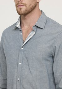 Chemise à boutons rayée bleu clair en tissu doux ; présente un col contrastant blanc et gris. Texture lisse, design ajusté.
