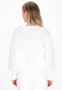 Weißer Strickpullover mit aufgeblähten Ärmeln, runder Halslinie und dekorativen Knöpfen an der Schulter; strukturierter Stoff mit lockerer Passform.