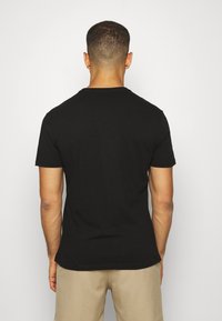 Camiseta de algodón negra con cuello redondo y mangas cortas, que presenta una textura suave y una silueta ajustada, vista desde la espalda.