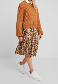 Brązowy sweter w prążki, spódnica plisowana w panterkę i białe trampki. Teksturowany materiał z długimi rękawami i luźnym krojem.