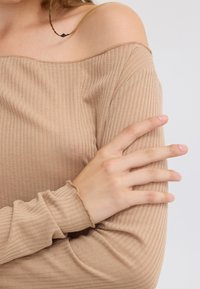 Beige ribbet langermet topp med avskåret skuldre. Har en avslappet passform og frynsede kanter ved mansjettene og utringningen.