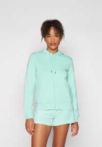 Felpa verde menta con zip, realizzata in tessuto morbido, con cappuccio, tasche frontali e polsini a costine; abbinata a pantaloni corti coordinati.