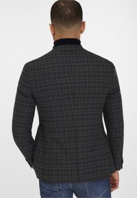 Tmavě kostkovaný blazer s přiléhavým střihem, zdobený zelenočernými vzory. Strukturované ramena a šálový límec dodávají celkovému vzhledu konečnou podobu.