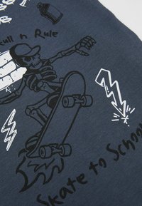 Dunkelblauer Stoff mit einem grafischen Druck eines Skeletts auf einem Skateboard, mit weißem Text und Blitzdesigns. Glatte Textur.