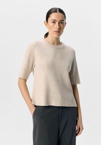 Lyse beige ribbet kortærmet sweater med rund hals, der har en afslappet pasform og en subtil tekstur; parret med mørkegrå løstsiddende bukser.