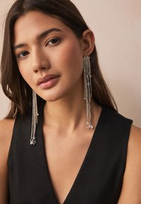 Silver chandelier earrings with cascading strands, featuring clear crystal accents. They hang below the earlobe, sparkling in light.