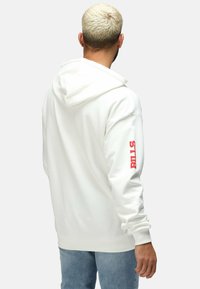 Weißer Hoodie mit einer Fronttasche und rotem Text "BILLS" am linken Arm. Hergestellt aus weichem Stoff mit einer lockeren Passform und mit Kordelzug-Kapuze.