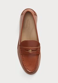 Brown leather loafer with a rounded toe, stitched detailing, and a decorative gold logo accent on the vamp. Smooth texture, slip-on design.