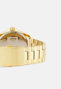 Goldfarbene Metalluhr mit rechteckigem Ziffernblatt, solidem Edelstahlboden und einem Gliederarmband-Design. Verfügt über einen Verschluss mit Markenlogo.