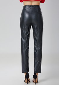 Pantalons en cuir noir avec une taille haute et une coupe droite. Texture lisse avec des coutures visibles ; associés à des chaussures à talons hauts noires.